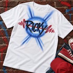 Styling mockup of a white Ricky airbrush name shirt with blue rays and a red heartbeat, on painted red brick beside cropped jeans, red high-top sneakers and a red cap. Shirt sold separately.